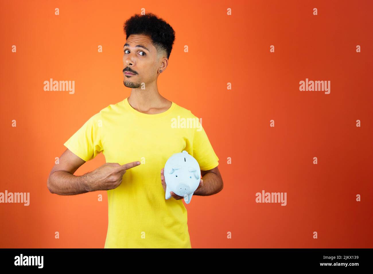 Bell'uomo nero che tiene una Piggy Bank isolato su Orange. Foto Stock