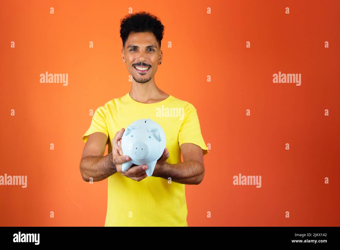 Bell'uomo nero che tiene una Piggy Bank isolato su Orange. Foto Stock