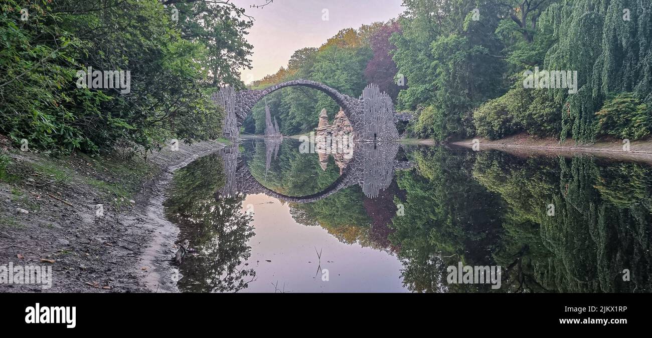 Un riflesso di un ponte e alberi in acque calme Foto Stock