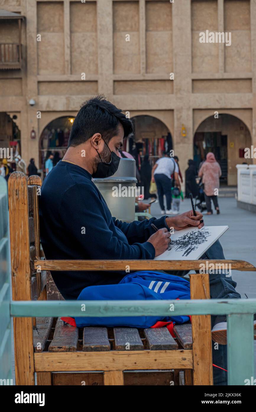 Primo piano verticale di un ragazzo seduto su una panchina mentre si disegna in Souq Waqif Doha, Qatar Foto Stock