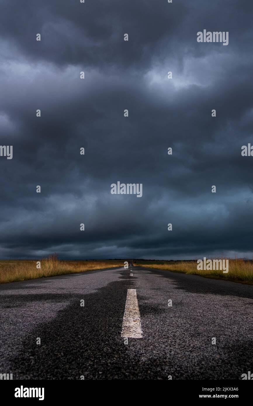 Un tratto verticale di una strada diritta attraverso i campi della campagna sotto il cielo nuvoloso Foto Stock