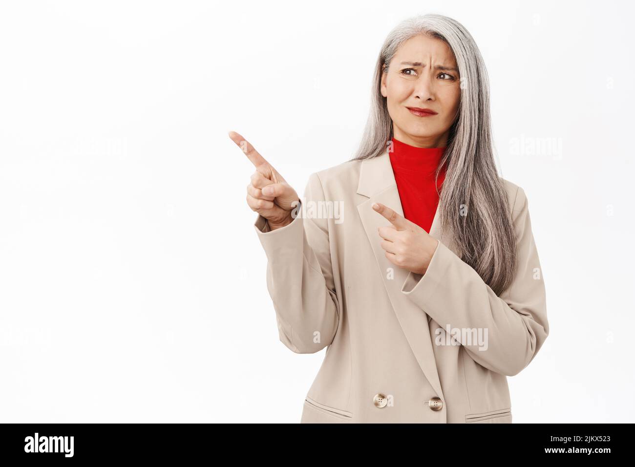 Donna d'affari anziana asiatica, imprenditore femminile che punta a sinistra con volto deluso, in piedi sconvolto contro sfondo bianco Foto Stock