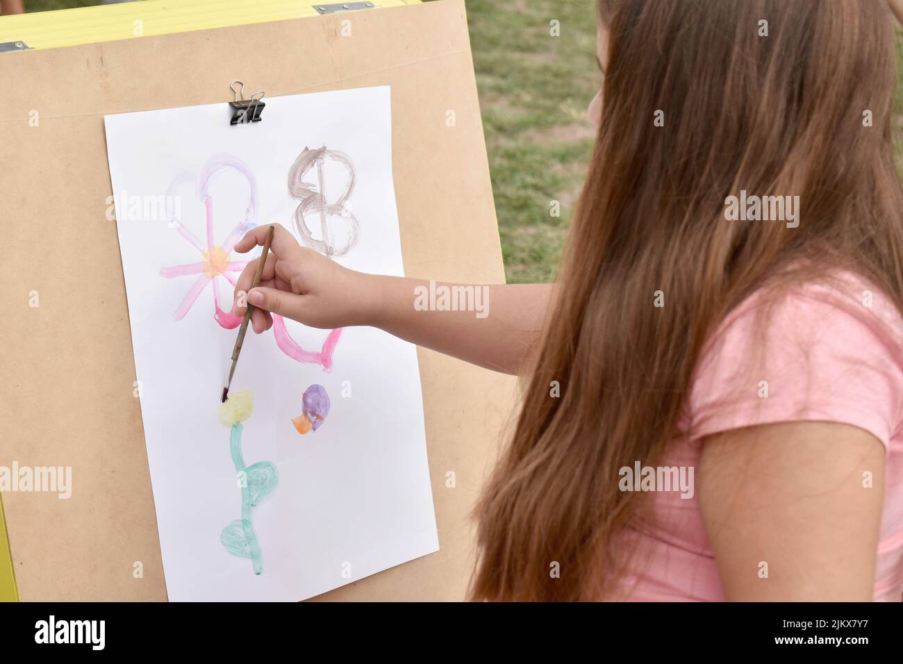 una ragazza dipinge fiori su una carta all'aperto, luce naturale Foto Stock
