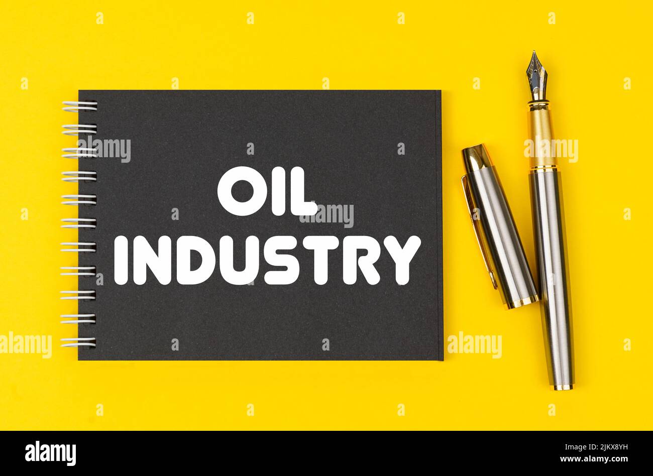 Concetto di business e finanza. Su uno sfondo giallo si trova una penna e un notebook nero con l'iscrizione - industria petrolifera Foto Stock