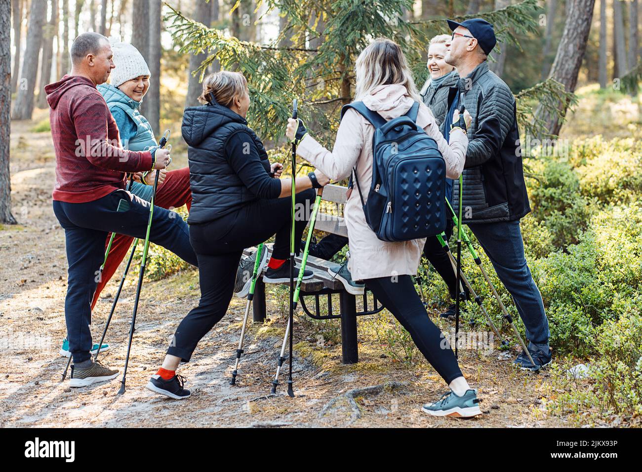 Gruppo persone che imparano a fare Nordic Walking con bastoni da trekking nella foresta, stand una gamba sulla panca. Stile di vita sano Foto Stock