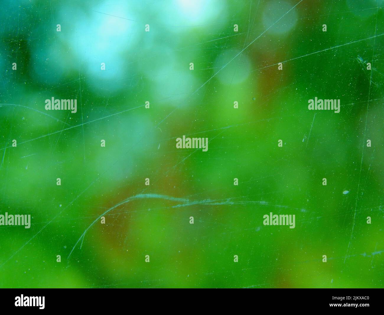 Primo piano di un vetro trasparente con graffi su uno sfondo verde sfocato Foto Stock