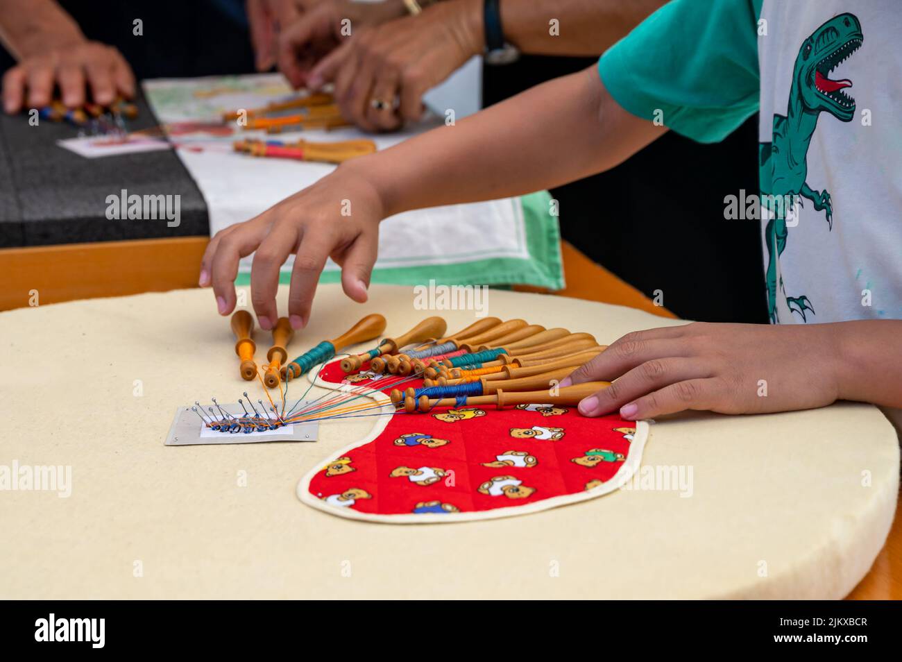 Mani di bambino e adulto che fanno merletto della bobina. Fili colorati di pizzo. Abilità e creatività. Foto Stock