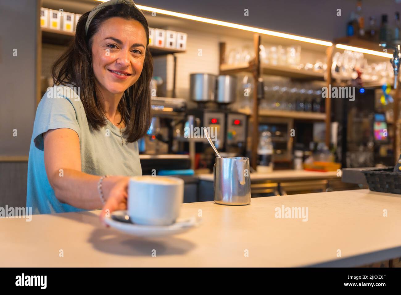 Cameriera sorridente nella caffetteria con il caffè preparato consegnandolo al cliente, le restrizioni dovute al covid sono rimosse e l'uso obbligatorio o Foto Stock