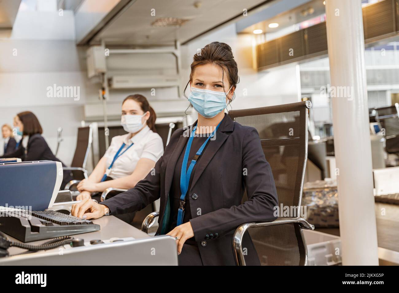 Donna dipendente della compagnia aerea che indossa la maschera facciale mentre lavora al banco check-in della compagnia aerea in aeroporto Foto Stock