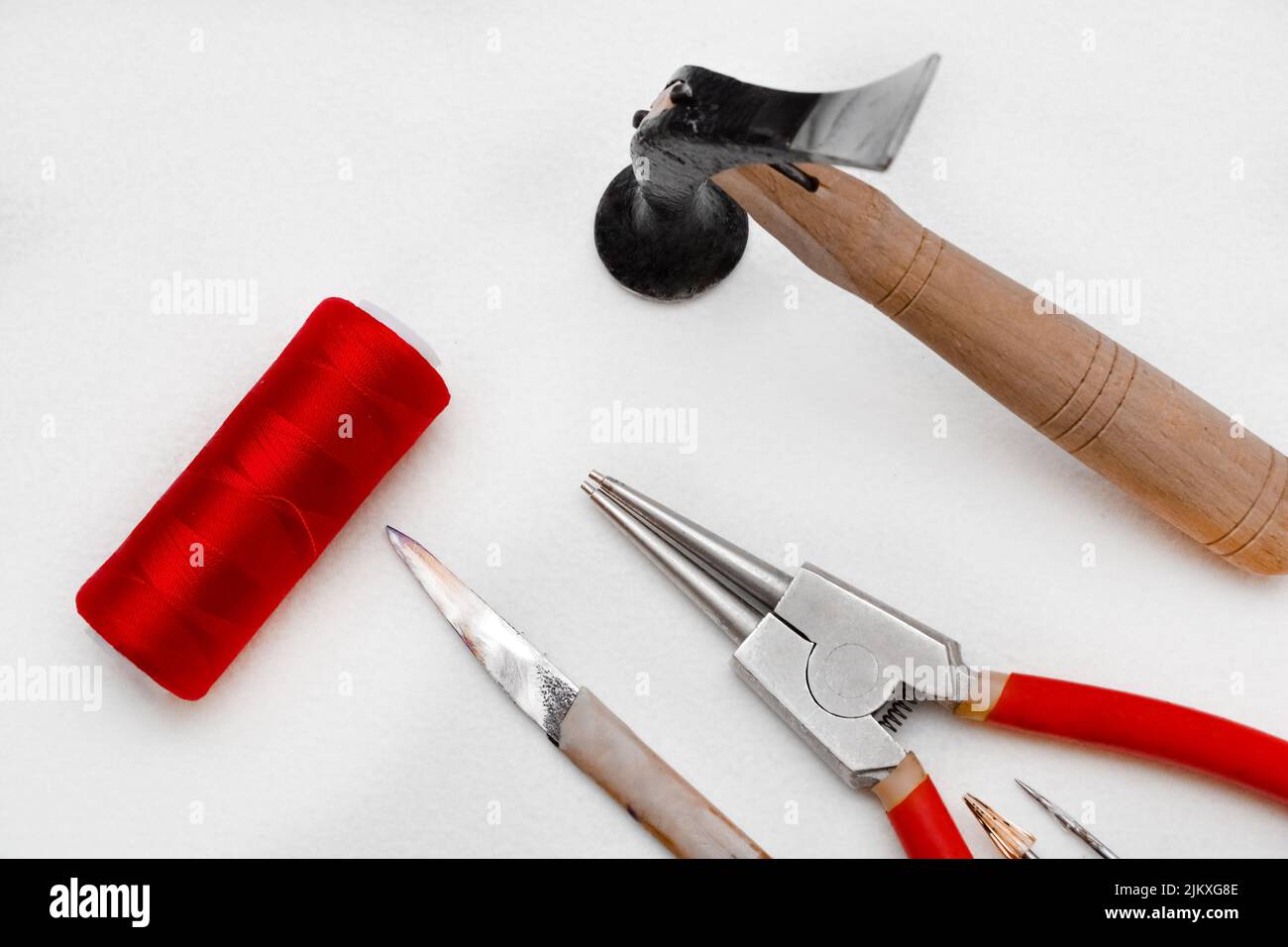Un primo piano degli strumenti isolati su sfondo bianco. Il martello, le pinze per anelli elastici, il coltello, la filettatura rossa. Foto Stock
