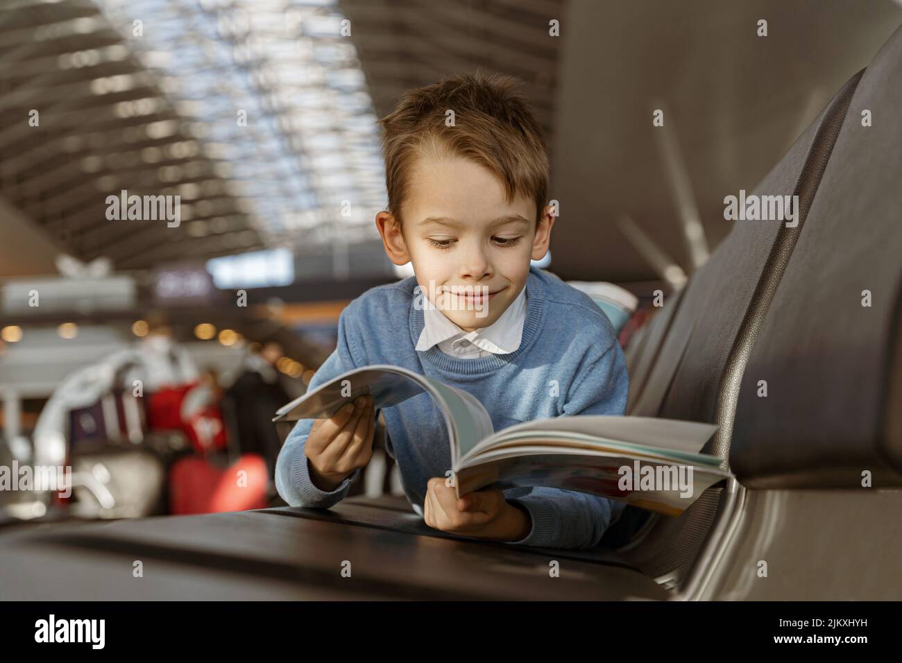 Il ragazzino legge un libro nella sala d'attesa dell'aeroporto prima del volo Foto Stock