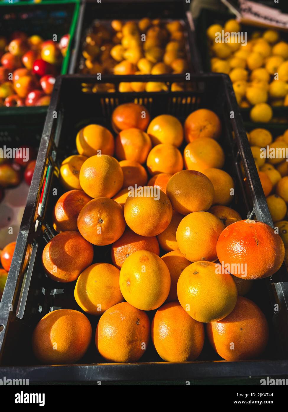 Un primo piano di arance fresche mature in un cesto di plastica nera in un mercato locale in una giornata di sole con sfondo sfocato Foto Stock