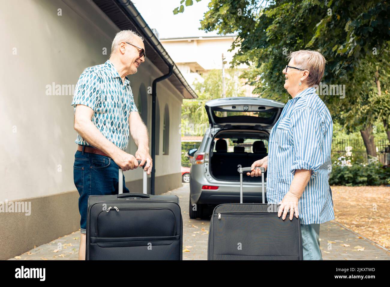 Coppia anziana che va in vacanza e che mette i bagagli o le borse di viaggio nel bagagliaio dell'automobile. Persone che partono in viaggio di ritiro con valigie e trolley in veicolo. Foto Stock