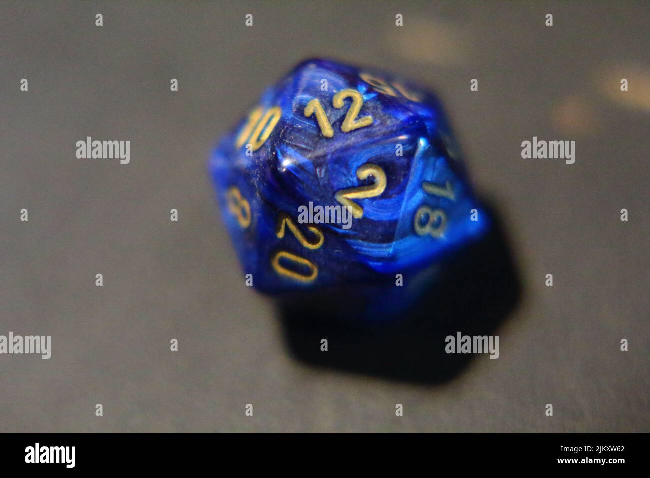 Un dado blu di metallo D20 con numeri d'oro sul tavolo Foto Stock