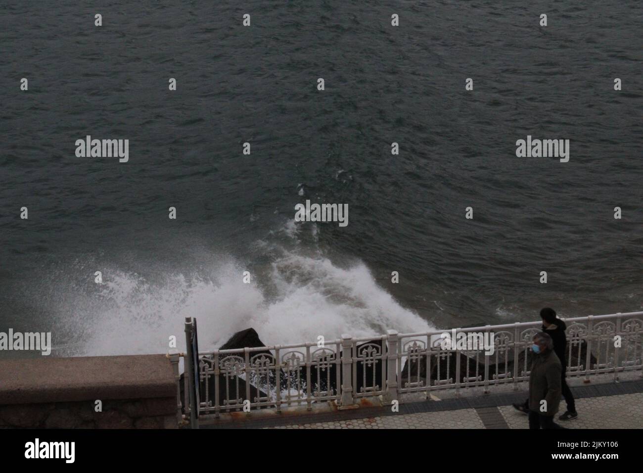 Una vista ad angolo alto di due persone che camminano vicino al molo vicino all'acqua che si schiantano sulle rocce Foto Stock