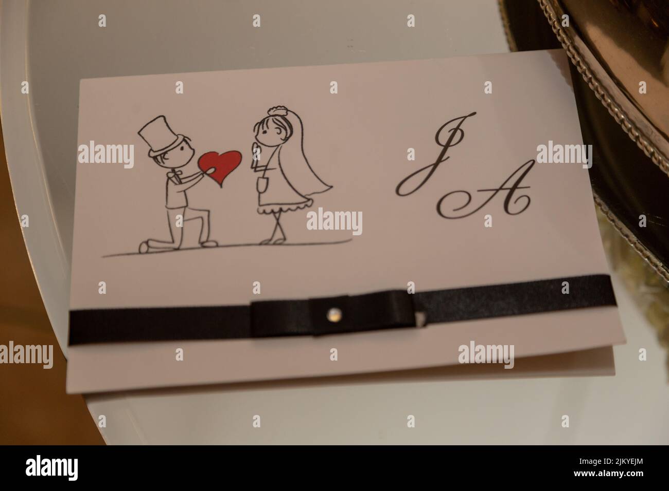 L'icona dello sposo che dà un cuore ad un'icona della sposa con le lettere J e Un disegno di un invito di nozze Foto Stock