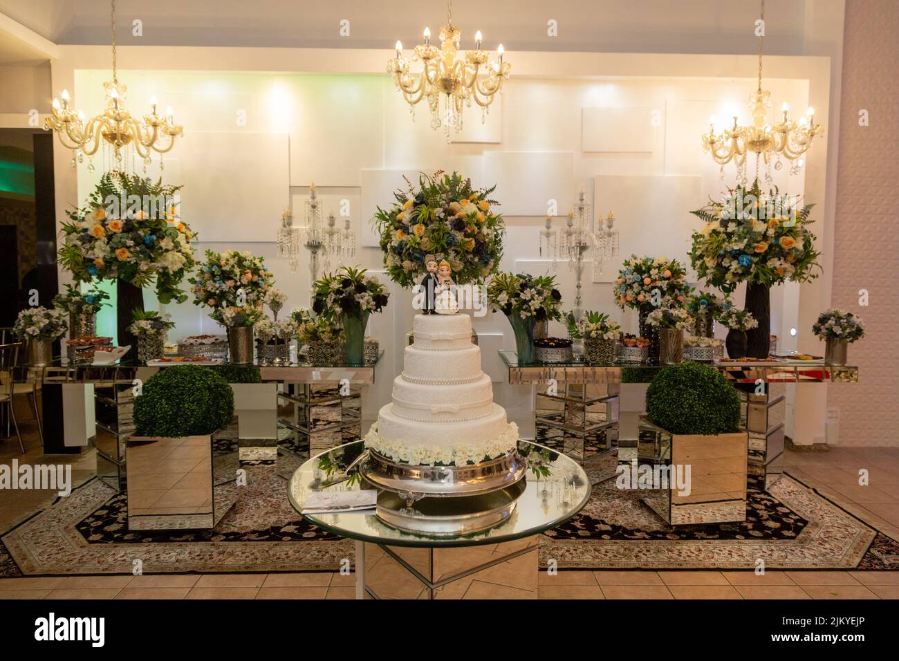 Una torta di nozze con figurine di sposa e sposo e un tavolo da pranzo dietro Foto Stock