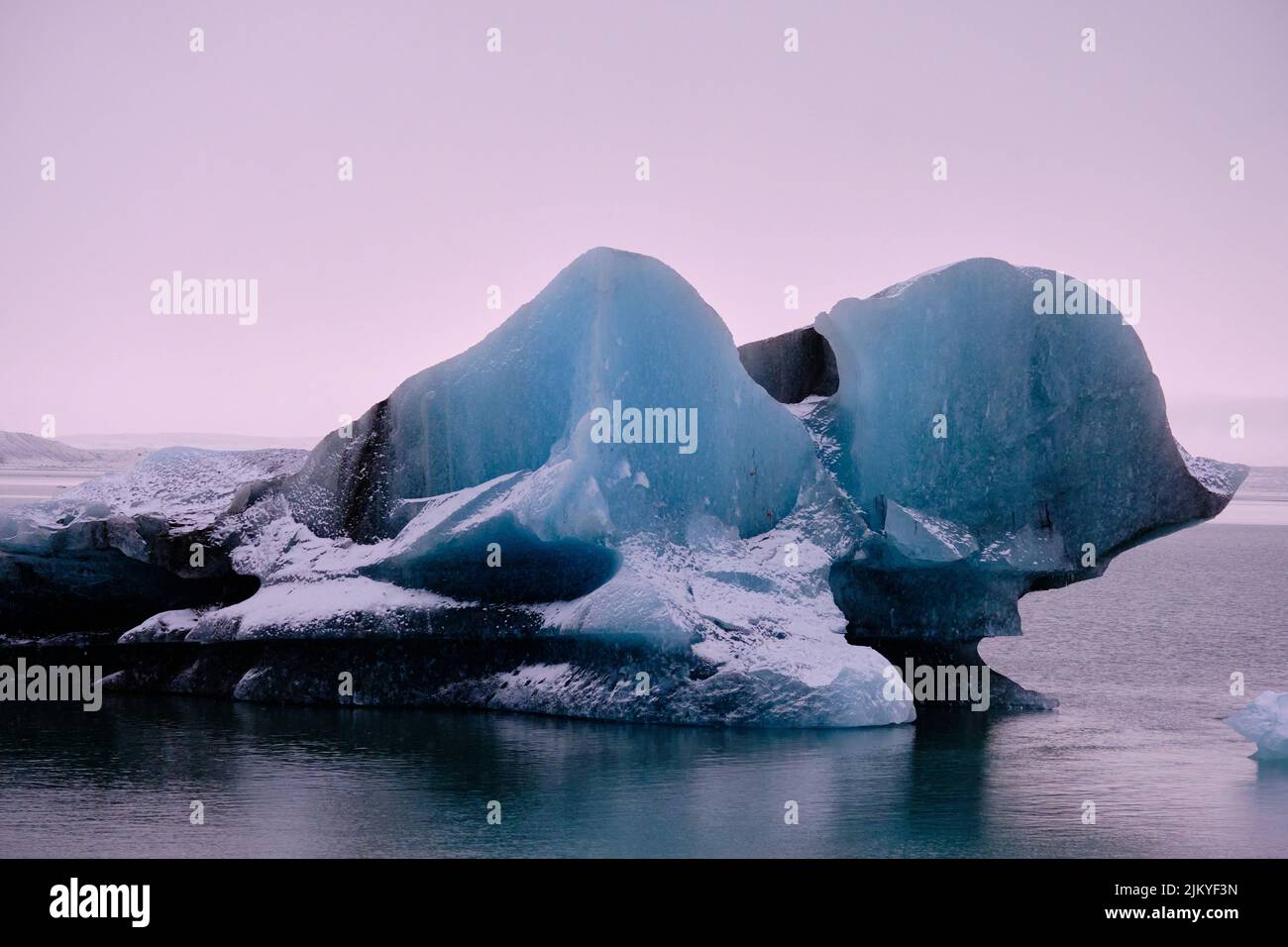 Grande iceberg blu con strisce nere che galleggiano sull'iceberg del ghiacciaio e il cielo rosa Foto Stock