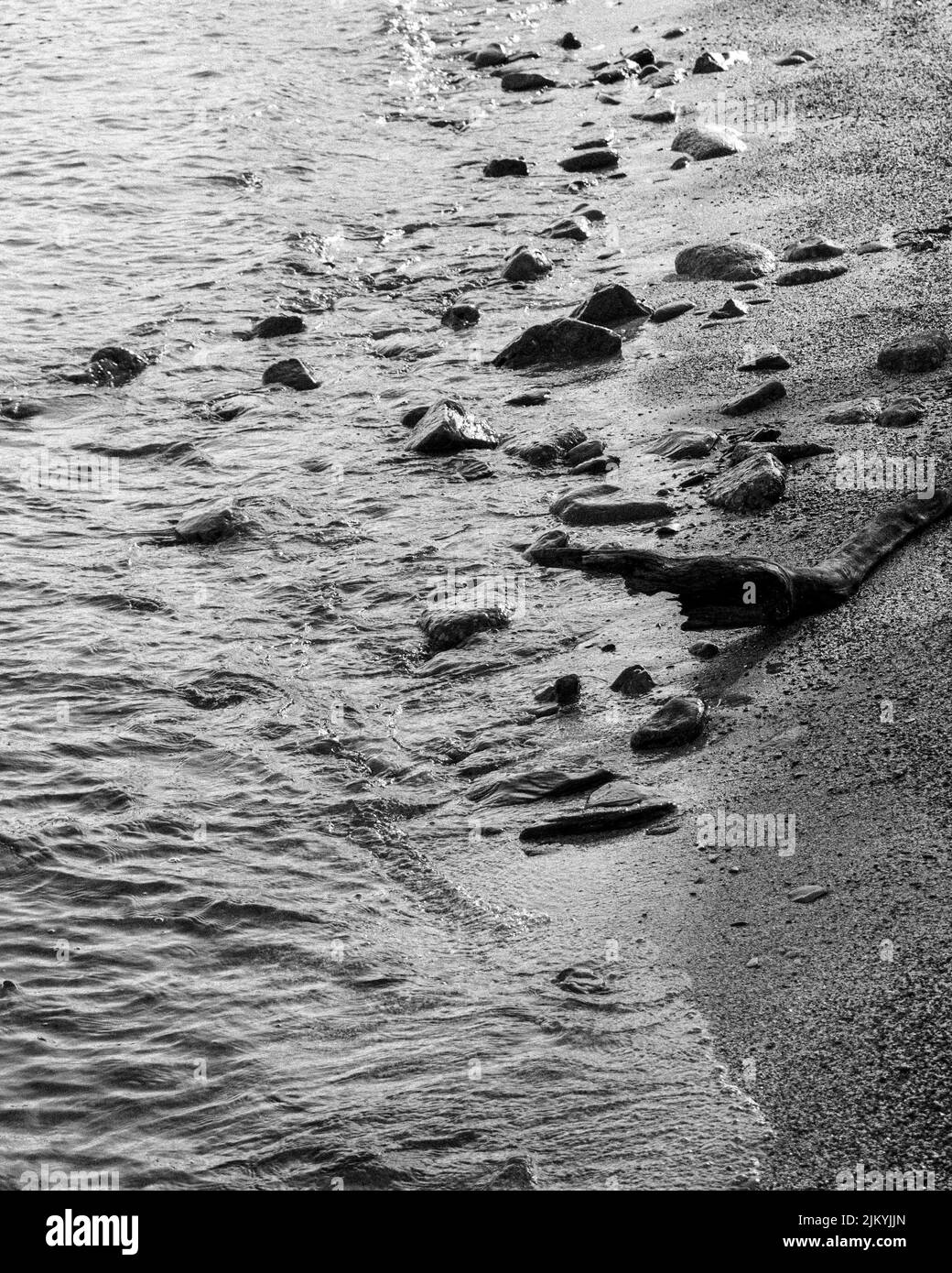 Una vista in scala di grigi di pietre e rocce sulla riva del lago che duca di giorno Foto Stock