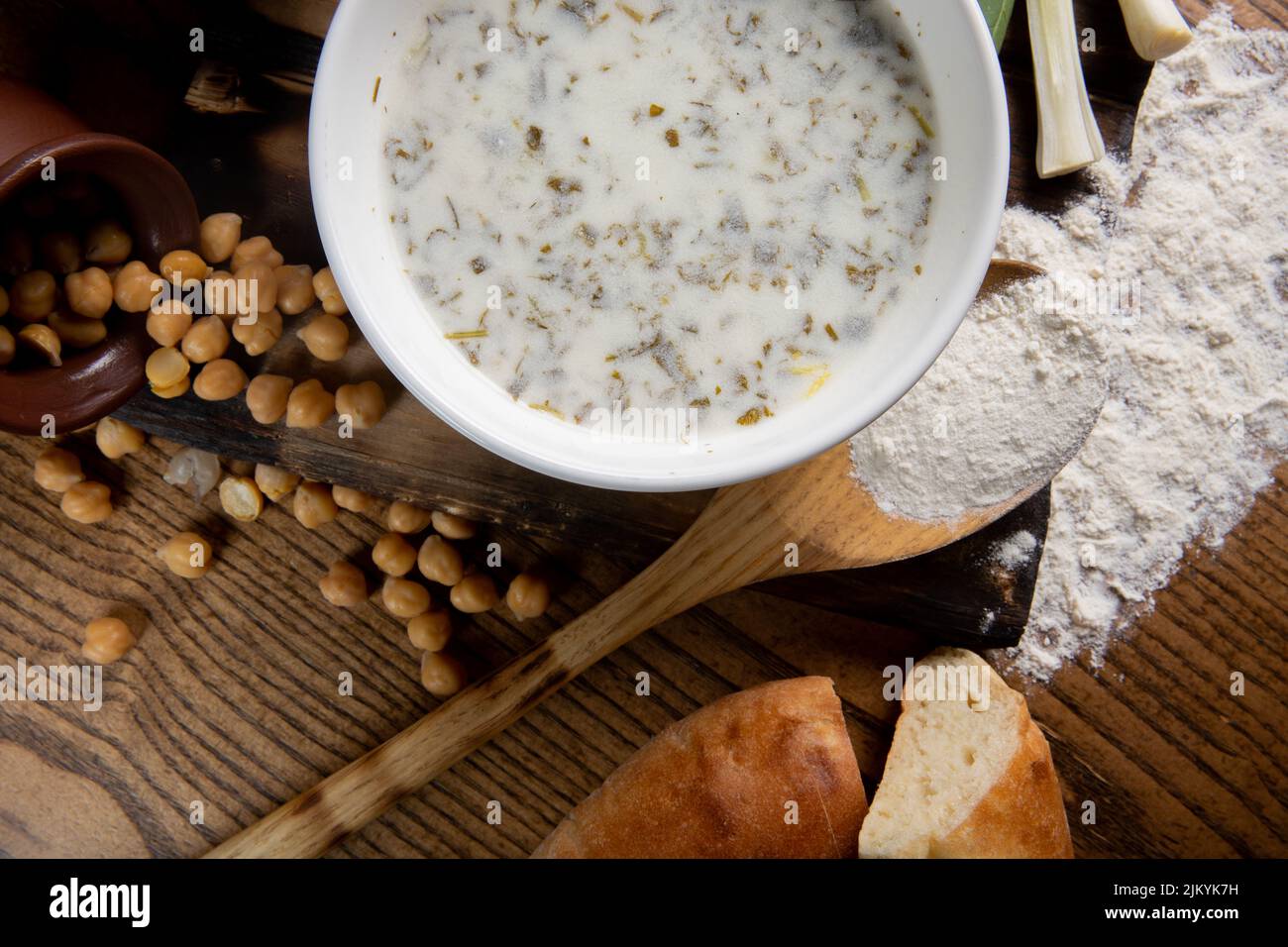 Una foto dall'alto di una zuppa di latte o di un porridge con fagioli che si versano da una pentola e pane su un tavolo di legno Foto Stock