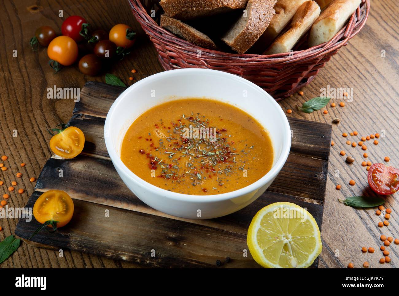 Una vista sulla zuppa gialla in una ciotola bianca con pomodori ciliegini, un limone e pane intorno ad essa Foto Stock