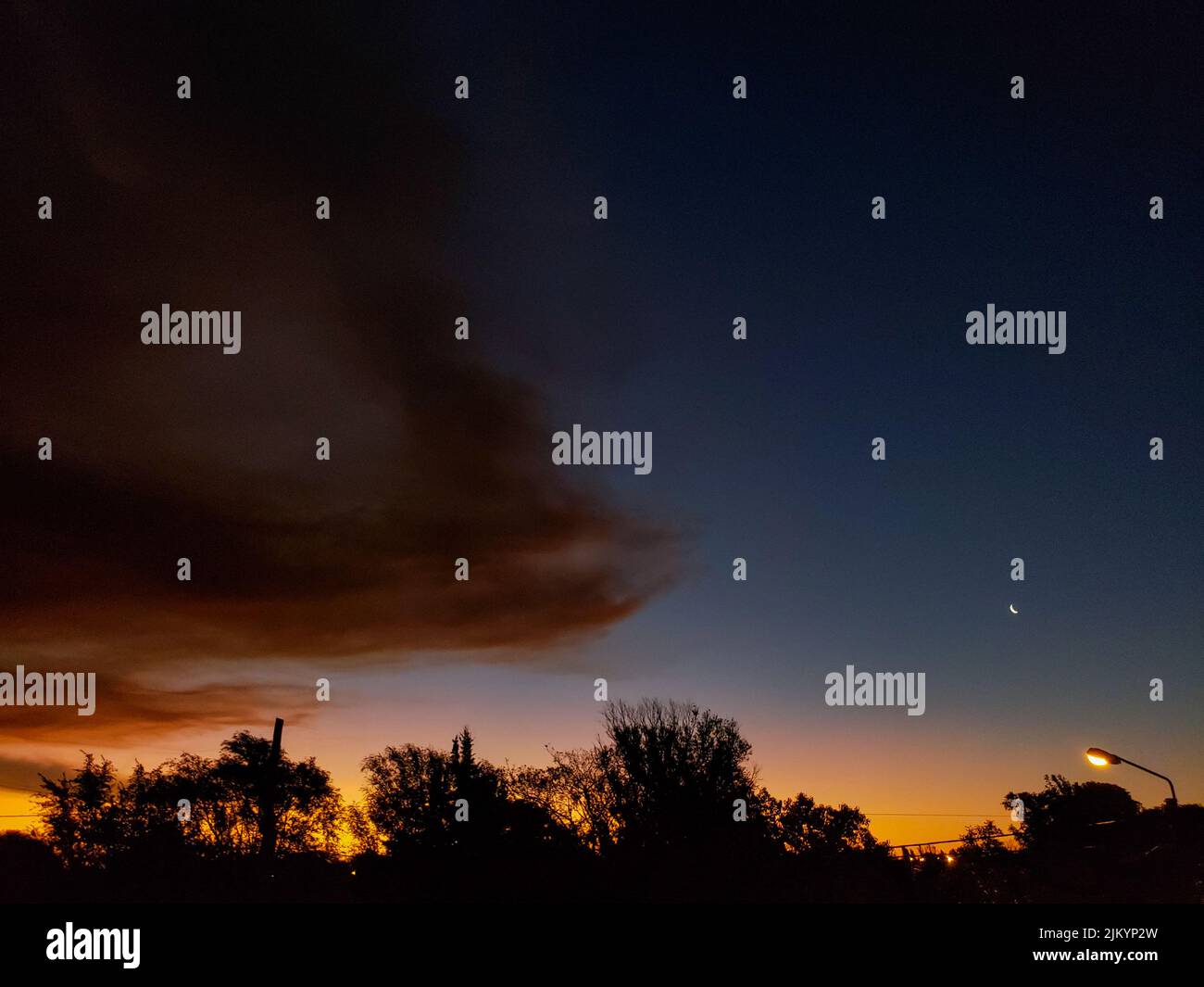 Uno scenario ipnotico del vivace tramonto con le nuvole, la luna crescente e le sagome degli alberi Foto Stock