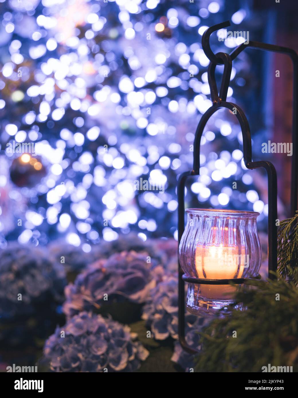 Un colpo verticale di una candela nella lanterna vicino all'albero di Natale con le luci alla vigilia Foto Stock