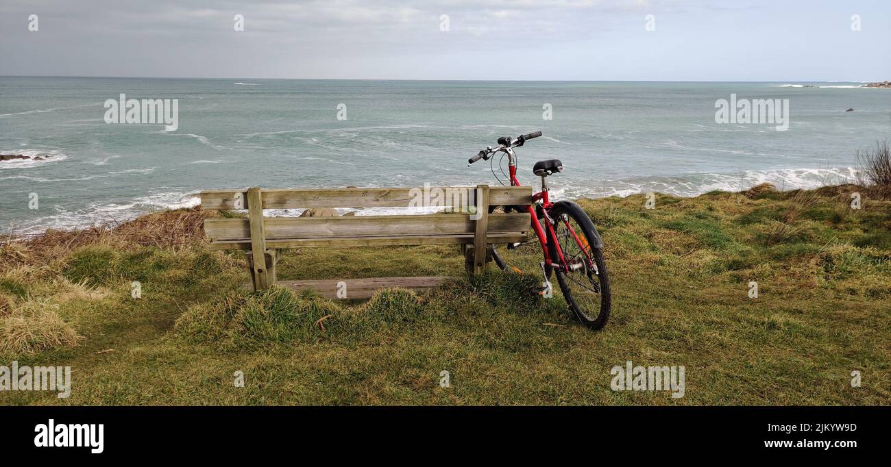 Una bicicletta vicino ad una panchina sulla riva di un mare Foto Stock