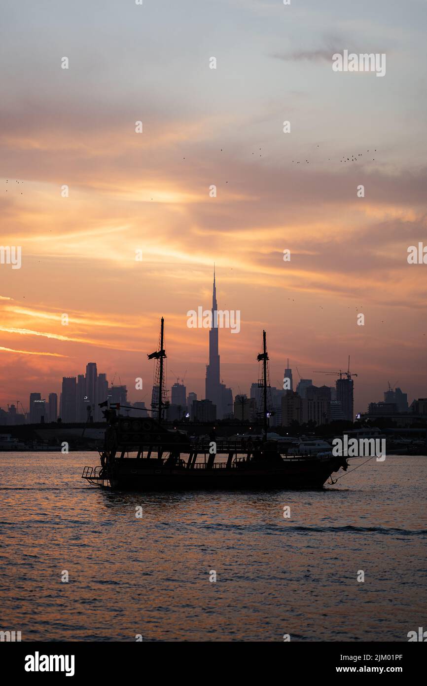 Una vista verticale mozzafiato di una nave nel Lago di Festival City con il paesaggio urbano di Dubai sullo sfondo del cielo al tramonto Foto Stock