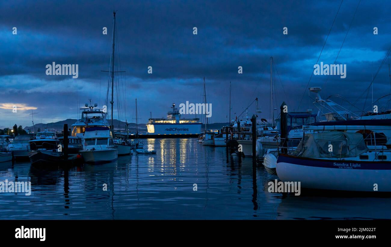 Un traghetto della British Columbia che passa dietro le barche attraccate in un porto turistico al crepuscolo. Foto Stock
