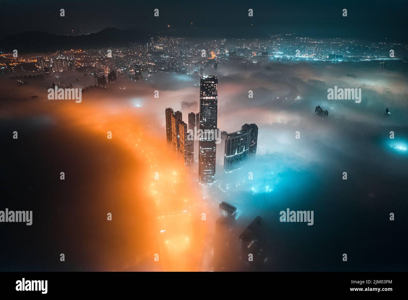 Un'immagine ad alto angolo di edifici alti in una città con luci luminose di notte e nebbia colorata intorno a loro Foto Stock