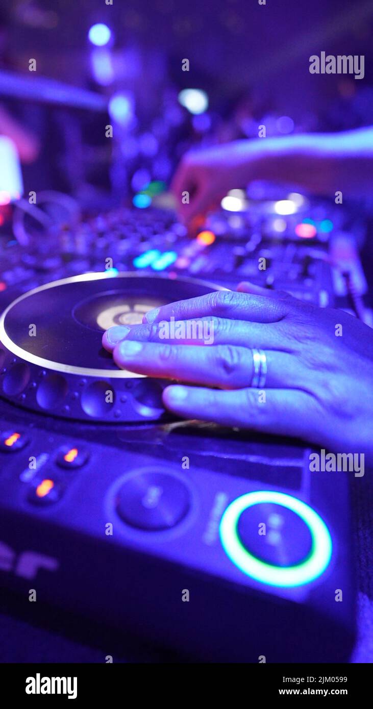Un primo piano verticale della mano di un DJ che controlla la musica sul set in una festa in discoteca Foto Stock