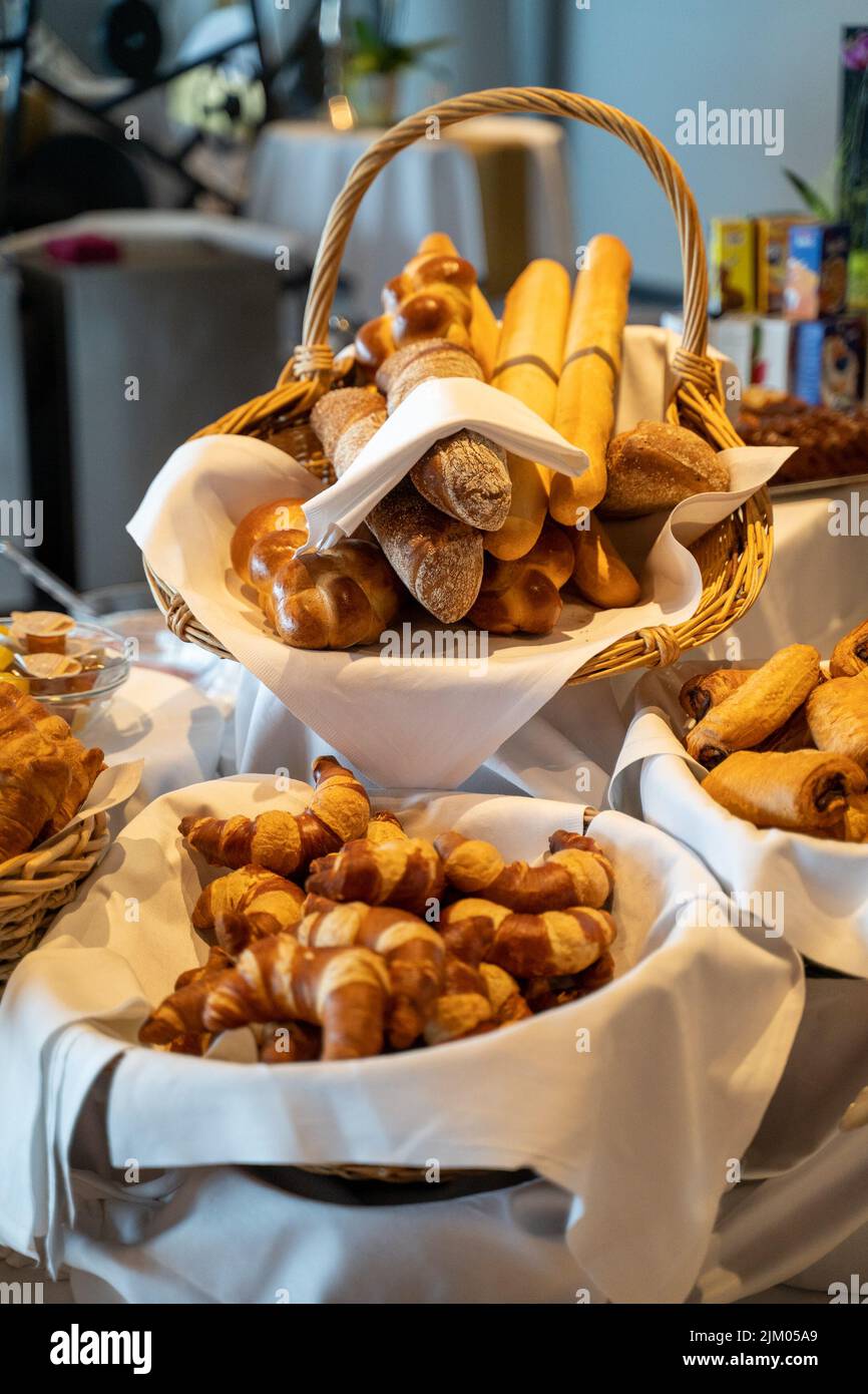Un primo piano verticale di un tavolo da ristorante con piatti e cesti pieni di bastoncini di pane e croissant Foto Stock