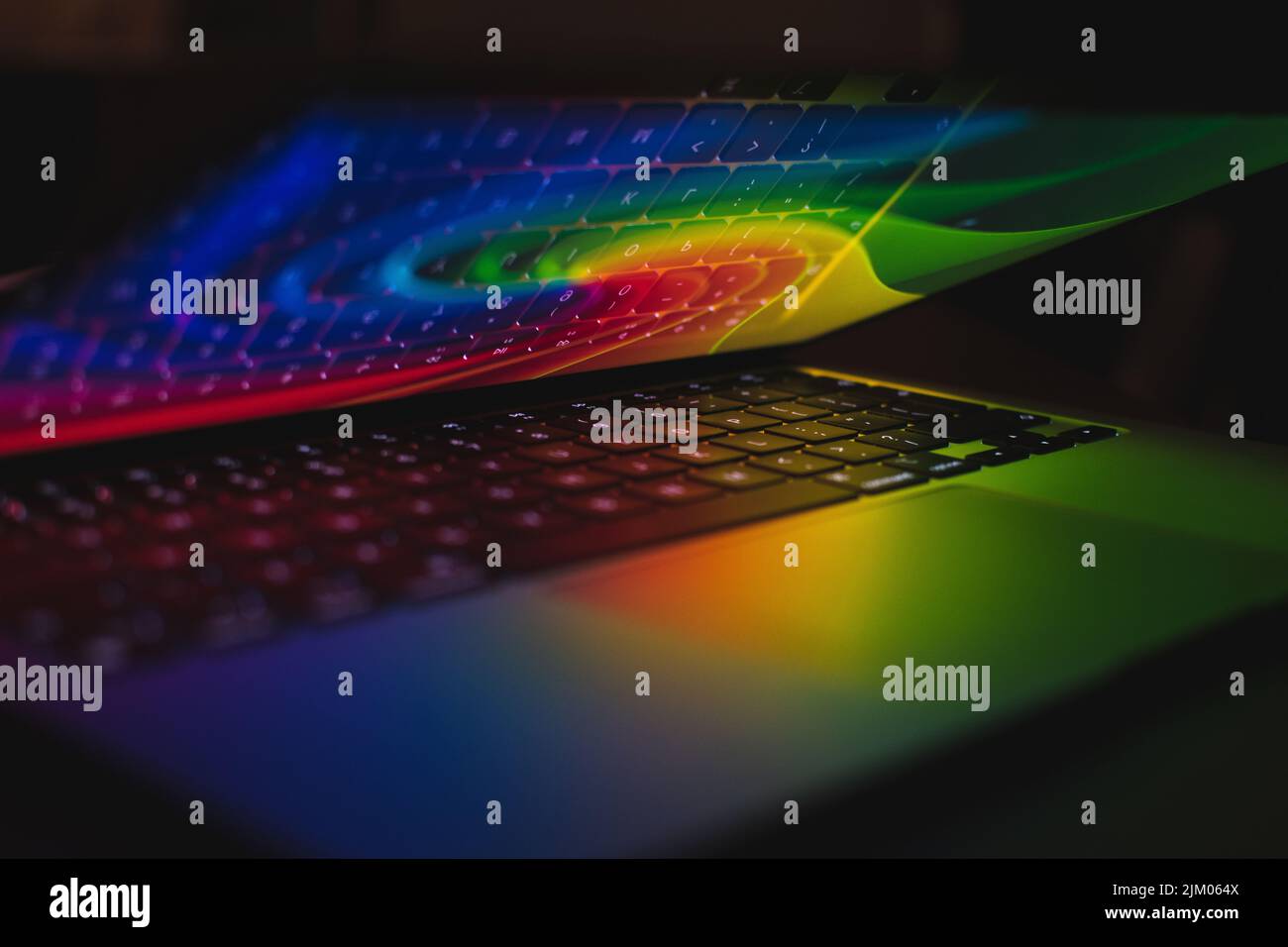 Un primo piano di un notebook aperto con luce arcobaleno e una tastiera che si riflette su uno schermo Foto Stock