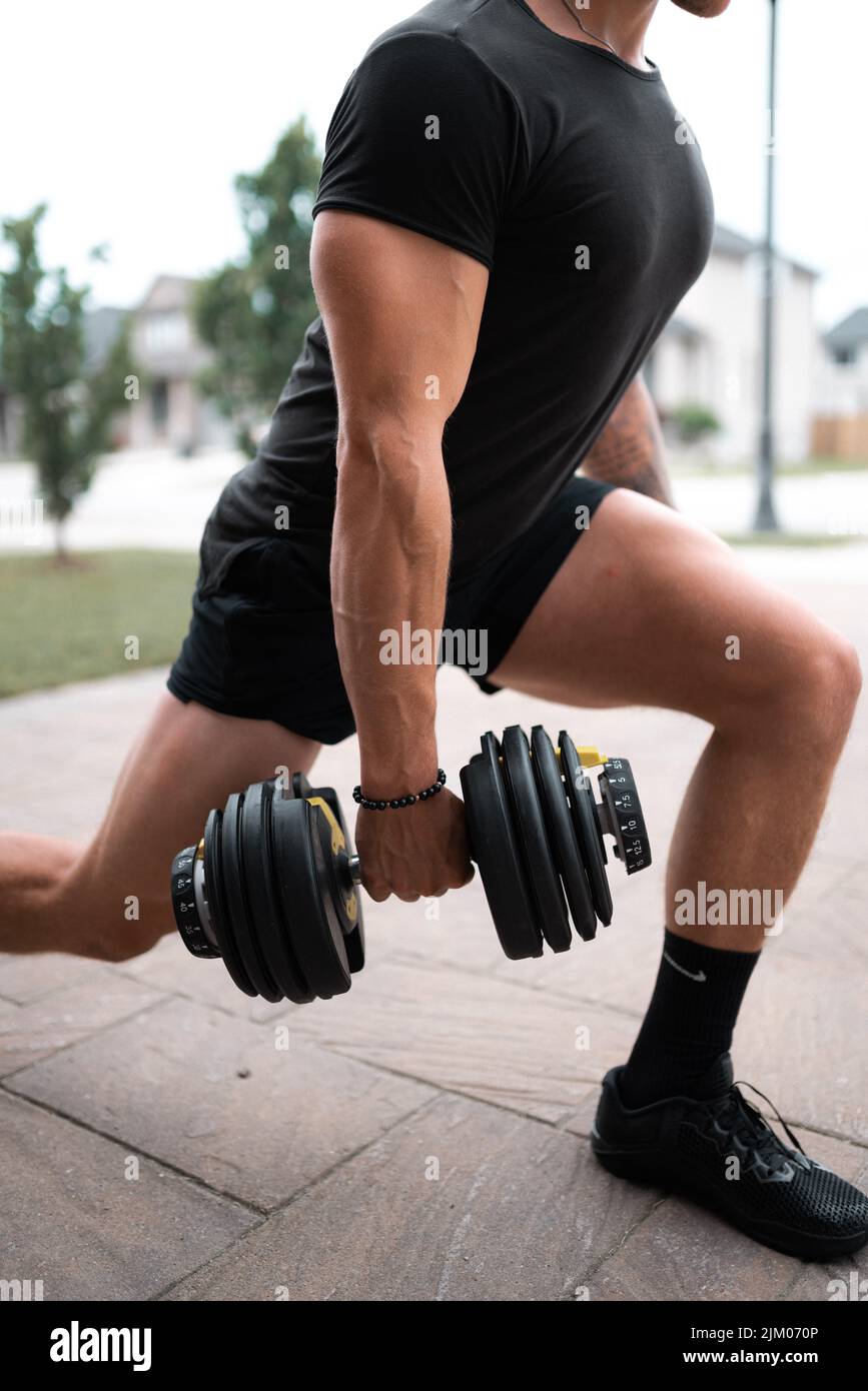 Il colpo verticale dell'uomo che indossa i vestiti della palestra che fa l'esercitazione con un dumbbell Foto Stock