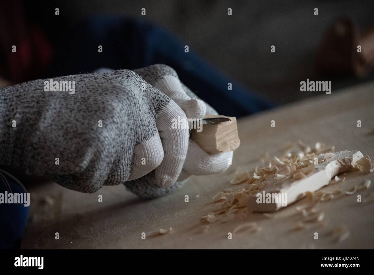 Primo piano di una persona che intagliava il legno con un coltello mentre indossava i guanti Foto Stock