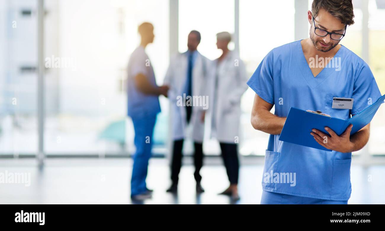 Giovane medico maschile che legge, tiene e guarda le informazioni sulla salute del paziente in un ospedale. Medico in piedi con i medici in Foto Stock