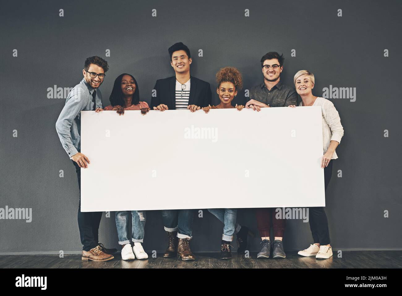 Un gruppo di professionisti che tiene una lavagna vuota o un cartello con spazio per la copia su sfondo grigio. Spazio di pubblicità di squadra vario o un posto vacante al loro Foto Stock