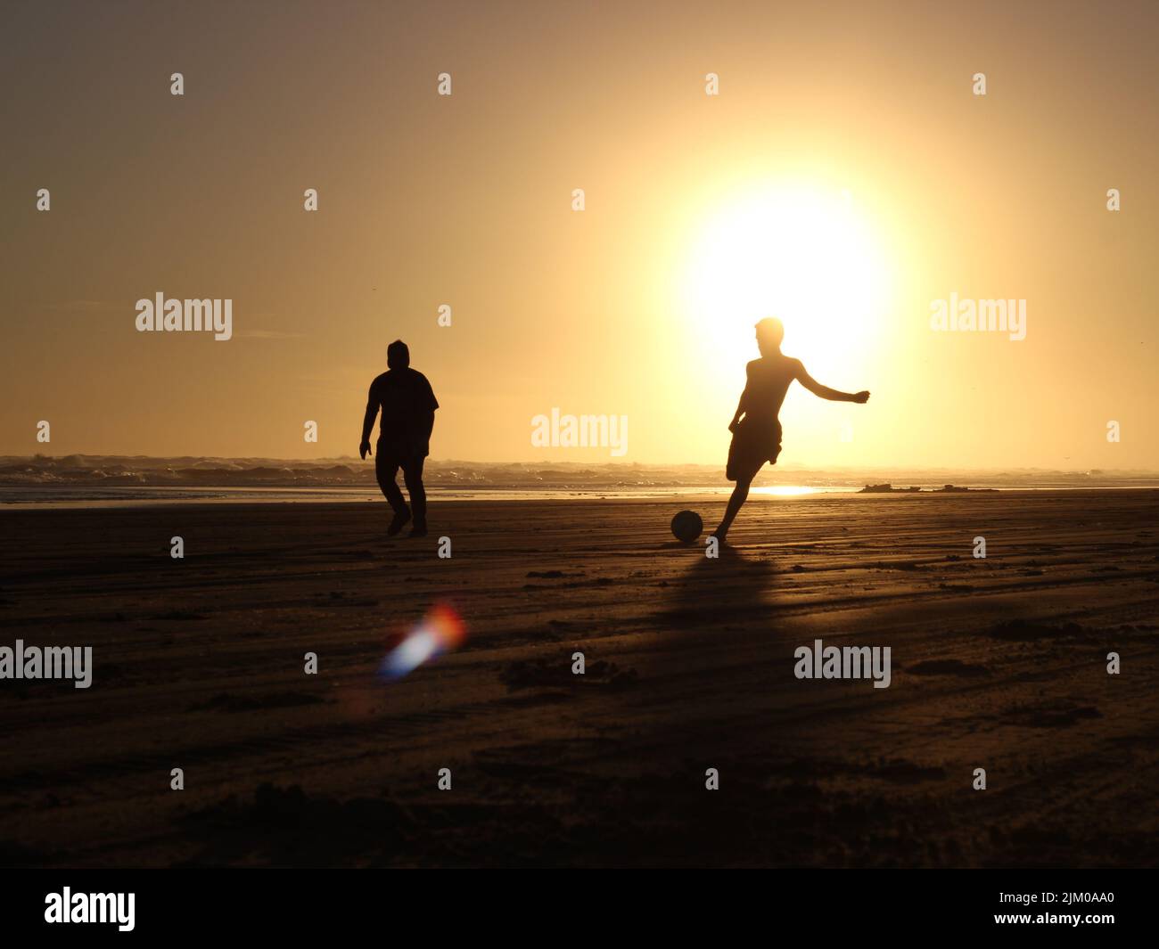 Due persone giocano sulla spiaggia sabbiosa al tramonto Foto Stock