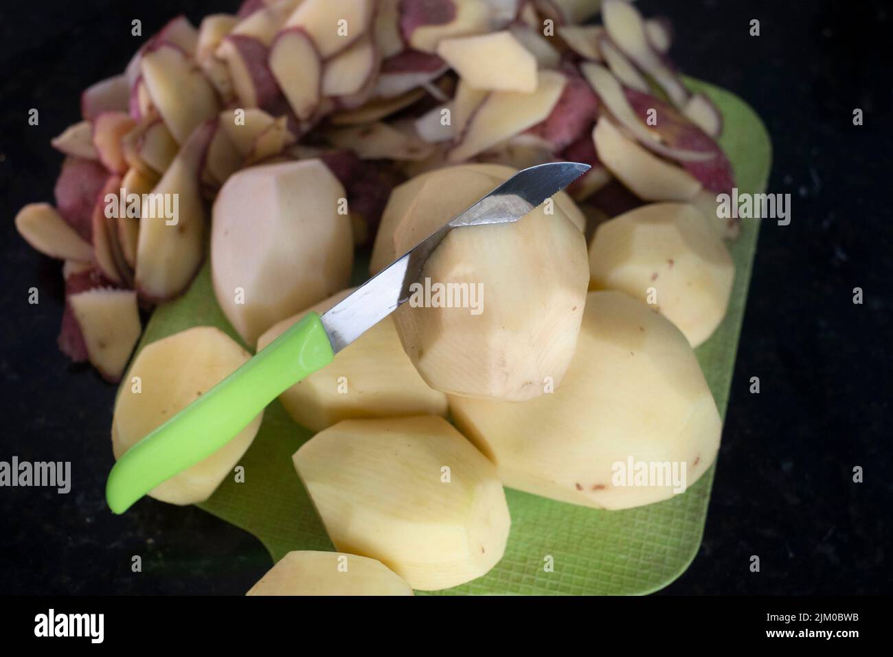 Un primo piano di patate sbucciate con un coltello verde Foto Stock