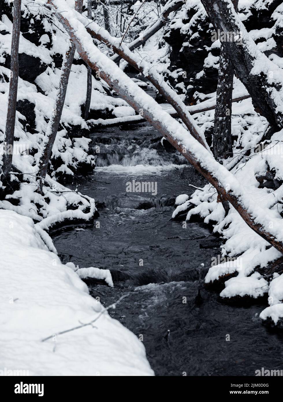 Uno scatto verticale di un fiume che scorre giù per le rocce ricoperte di neve in inverno Foto Stock
