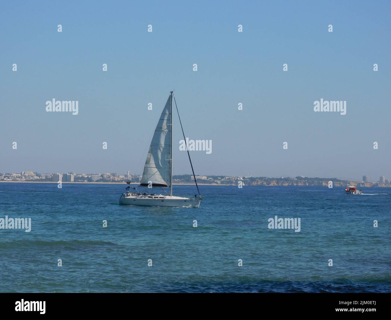 Un'immagine panoramica di una barca a vela bianca nel mare calmo sotto un cielo blu chiaro Foto Stock