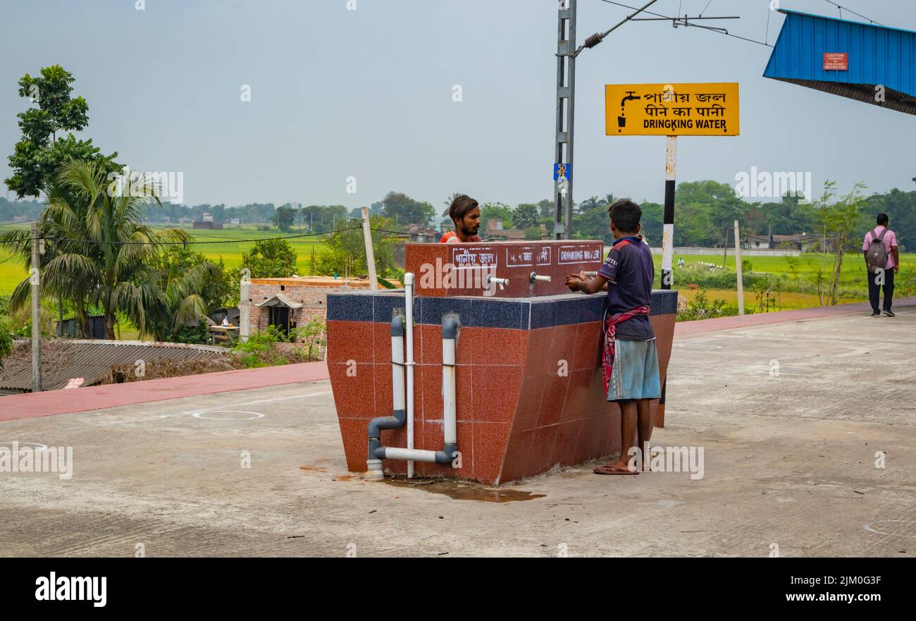 Due abitanti del villaggio che bevono acqua da un chiosco d'acqua alla stazione ferroviaria di Bardhaman del Bengala occidentale, India. Foto Stock