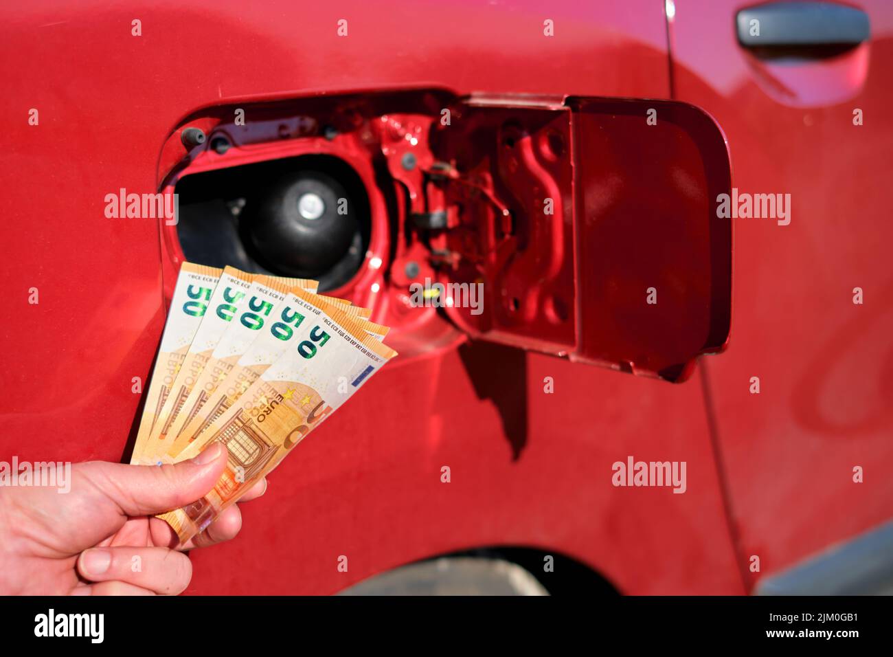 Primo piano di una mano che tiene un pacco di cinquanta banconote in euro davanti ad un serbatoio del combustibile aperto. Simbolo per l'aumento dei prezzi di trasporto della benzina e dell'automobile Foto Stock