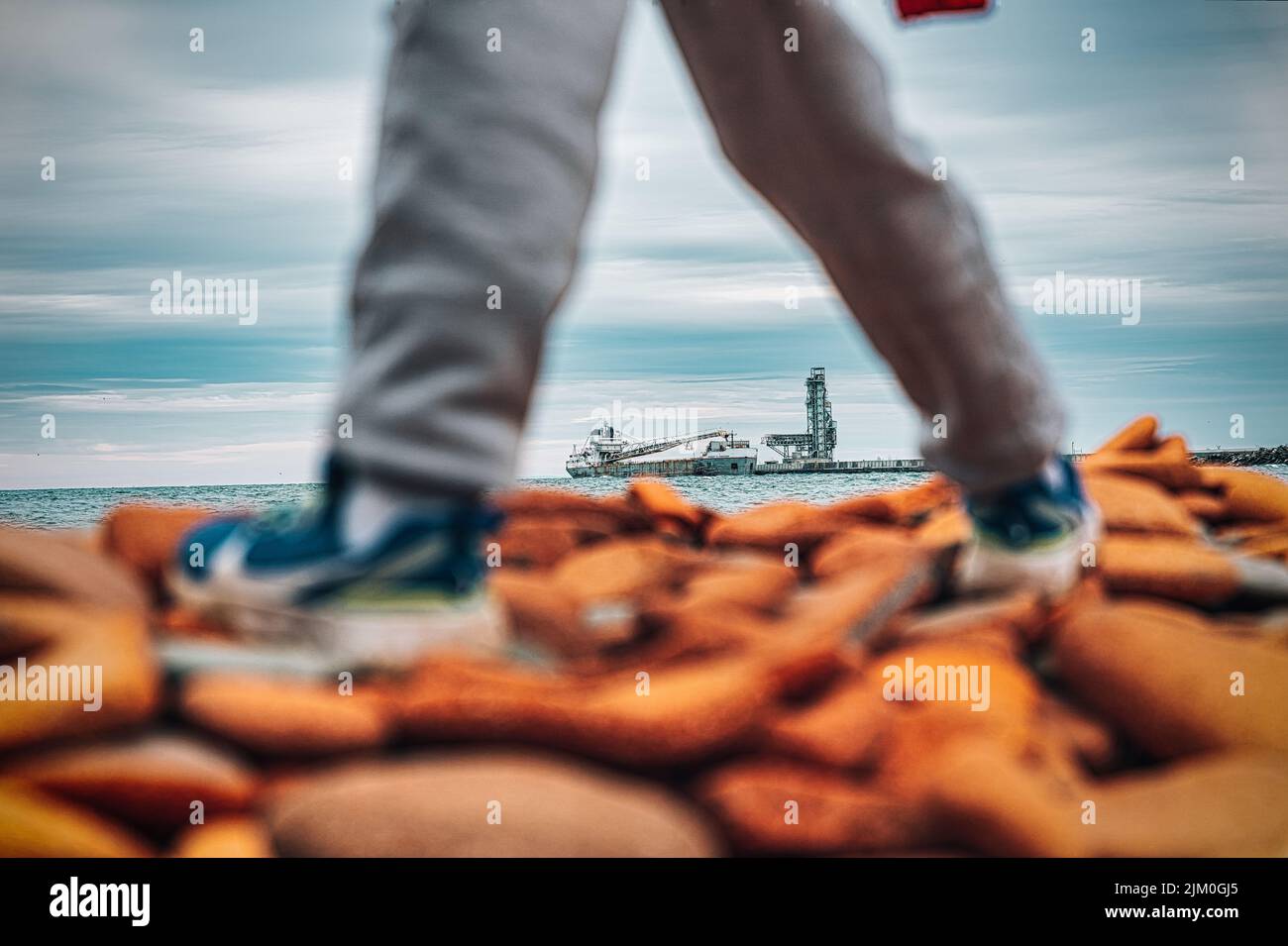 Un primo piano di gambe che camminano su una spiaggia rocciosa con ciottoli rossi in una giornata colma Foto Stock