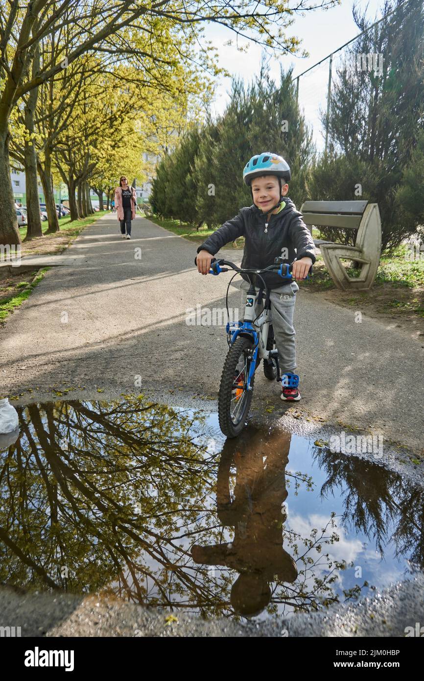 Un bambino con un casco di sicurezza seduto in bicicletta accanto a una pozzanghera nella zona di Orla Bialego Foto Stock