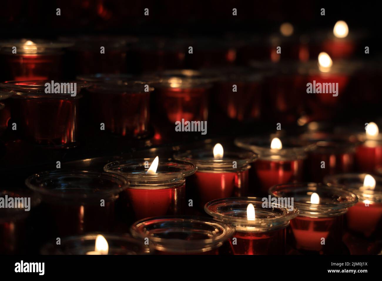 Una foto selettiva di righe di candele accese disposte in una stanza buia Foto Stock