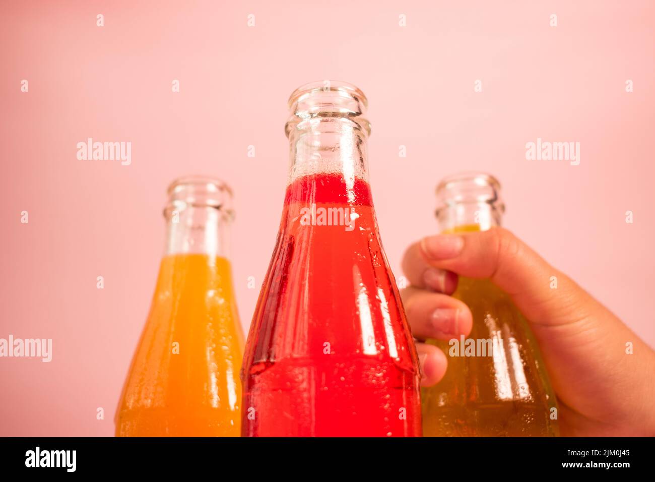 Un primo piano di tre bottiglie di vetro con bevande colorate e gustose su sfondo rosa Foto Stock