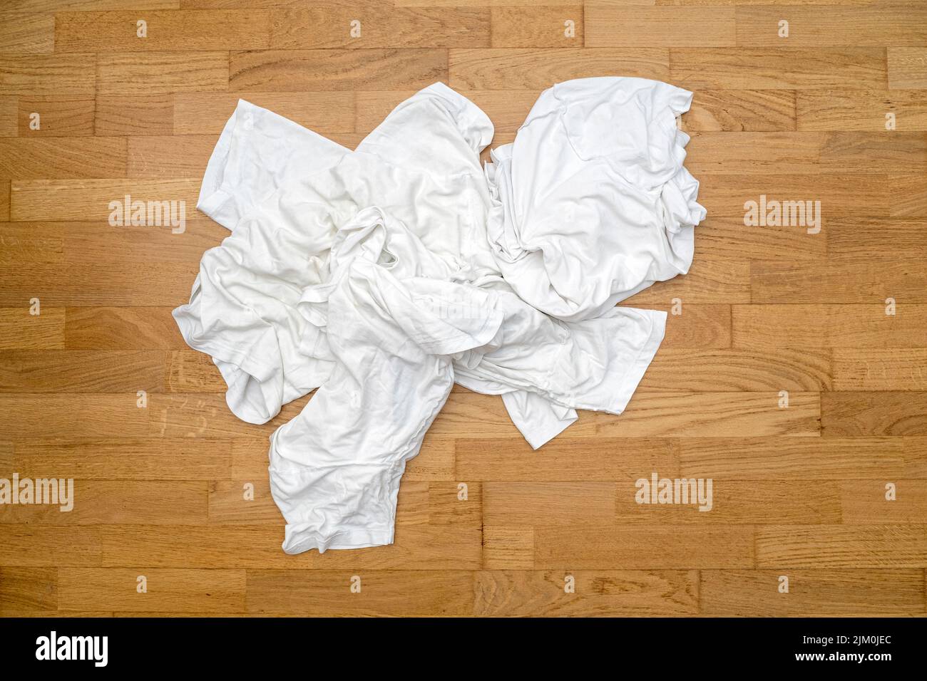 T-shirt bianche sporche e dissuasie per lo sport su pavimento in legno prima di lavarsi in lavanderia Foto Stock