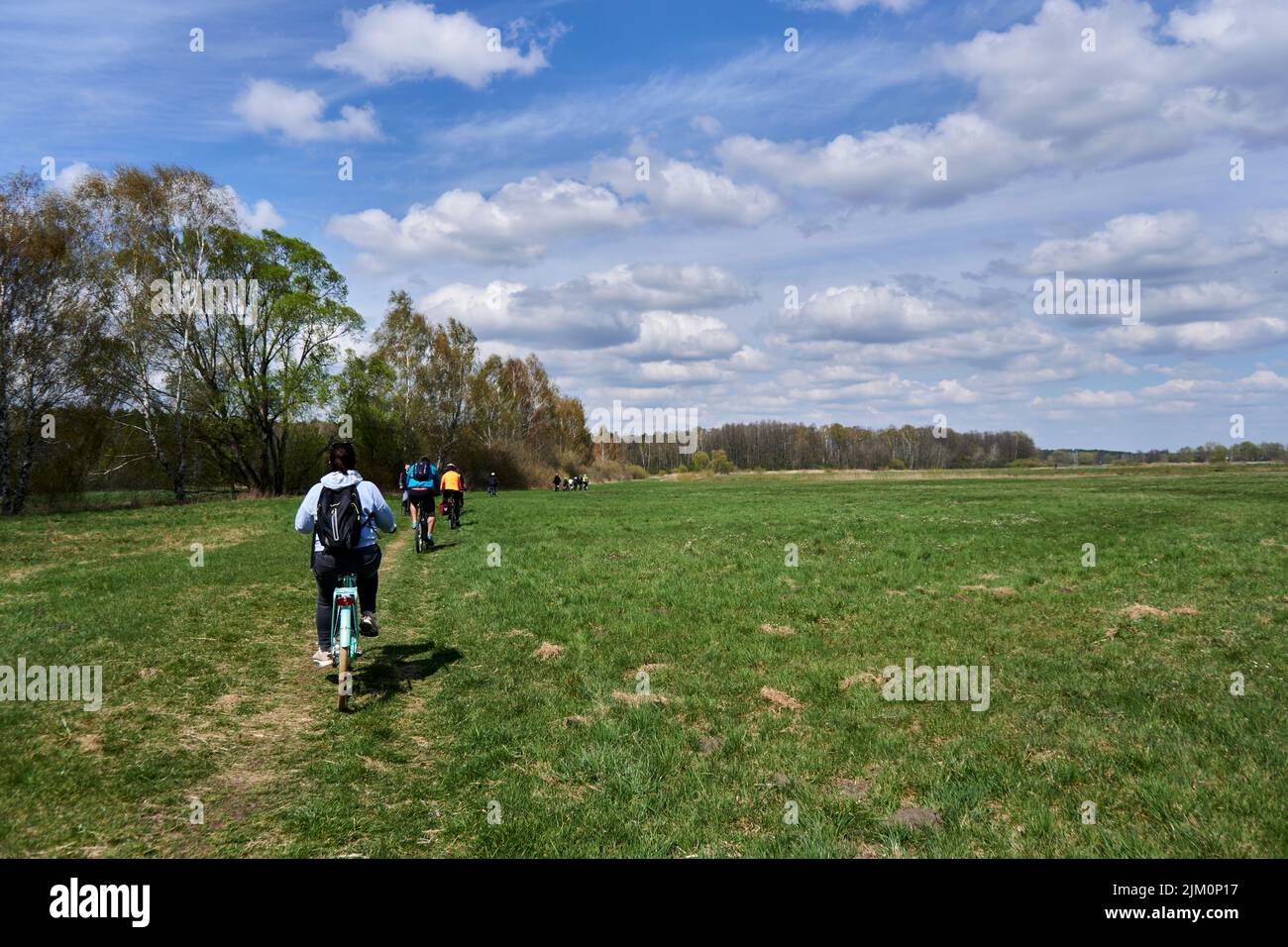 Un gruppo di persone in bicicletta su un prato verde con foresta durante una gita in bicicletta Foto Stock